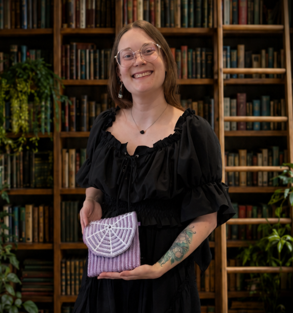 Amanda smiling while holding a purple crochet purse with a white spiderweb flap